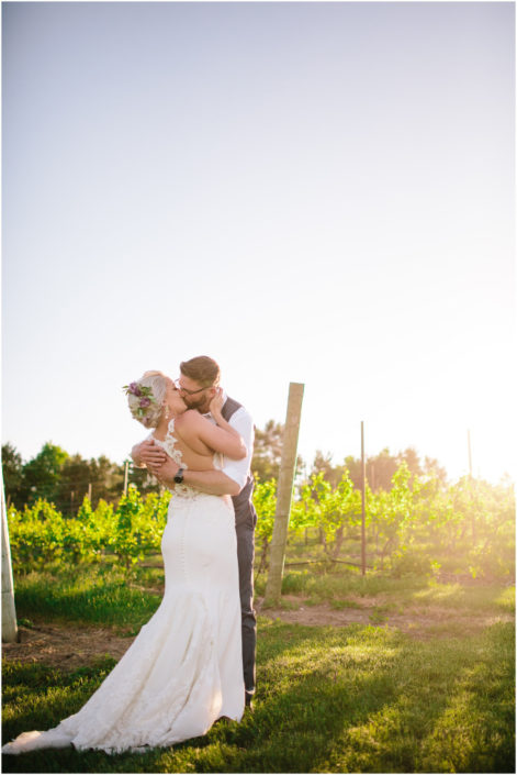 Bride and groom kissing in the vineyard in June.