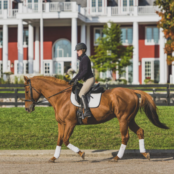 Woman riding a horse at the Stables at Black Star Farms with the Inn in the background.