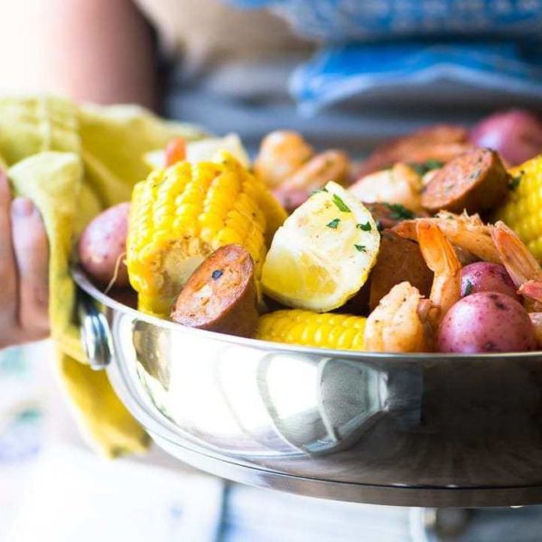 Person carrying a bowl with shrimp, potatoes, corn, lemon and parsley.