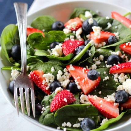 A spinach salad with fresh berries and feta cheese.