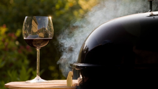 Image of a glass of wine next to a smoking grill.