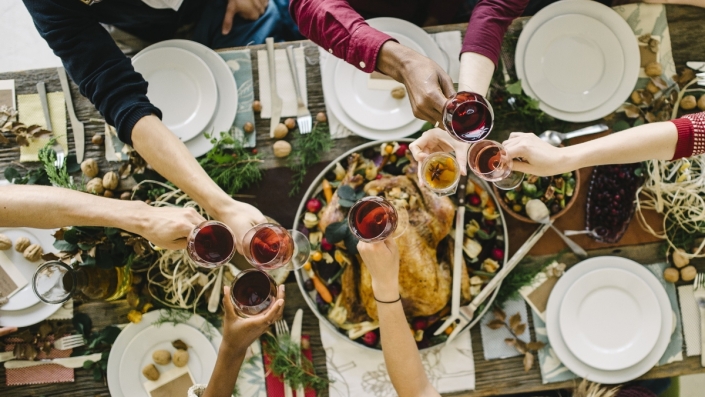 People clinking glasses of wine over a Thanksgiving table.