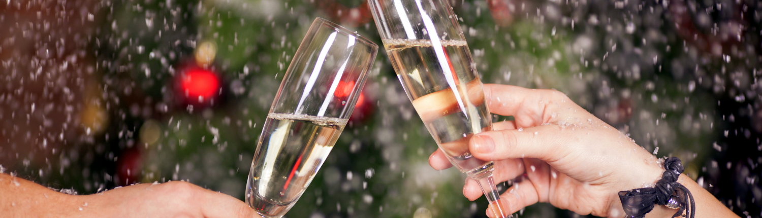 A sparkling wine toast with a Christmas tree in the background and snow falling.