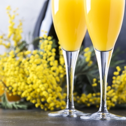 Two glasses of Mimosas with yellow flowers in the background.