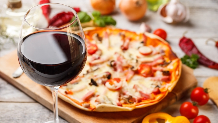 A glass of red wine with a pizza on a cutting board.