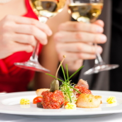 Couple clinking wine glasses over an attractive plate of food.