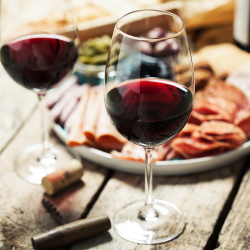 Two glasses of red wine with a meat and cheese board in the background.