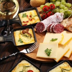 Raclette grill trays with cheese plus a glass of white wine.